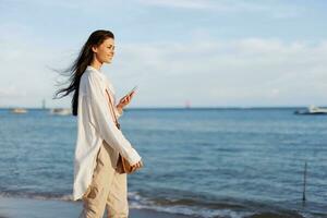 libero professionista donna con Telefono nel mano su vacanza a piedi su il spiaggia di il oceano nel Bali, contento viaggio e vacanza, mobile comunicazioni, Internet in linea foto