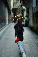 moda donna turista nel elegante Abiti nel un' giacca e rosso berretto in esecuzione giù il stretto strada di il città Sorridi e felicità viaggio, francese stile, cinematico colore. foto