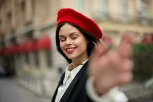 moda donna Sorridi con denti in piedi su il strada nel davanti di il città turista Seguire me elegante Abiti con rosso labbra e rosso berretto, viaggiare, cinematico colore, retrò Vintage ▾ stile, urbano moda. foto