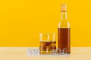 bicchiere di whisky con cubetti di ghiaccio e bottiglia su sfondo giallo