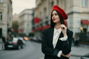 moda donna ritratto in piedi su il strada nel davanti di il città nel elegante Abiti con rosso labbra e rosso berretto, viaggiare, cinematico colore, retrò Vintage ▾ stile, urbano moda stile di vita. foto