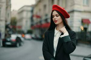 moda donna ritratto bellezza in piedi su il strada nel davanti di il città nel elegante Abiti con rosso labbra e rosso berretto, viaggiare, cinematico colore, retrò Vintage ▾ stile, urbano moda stile di vita. foto