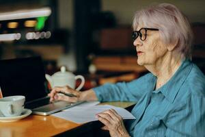 contento anziano donna nel un' bar un' tazza di bevanda il computer portatile stile di vita inalterato foto