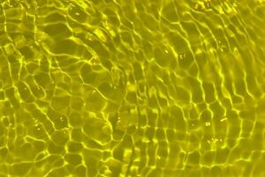 giallo acqua con increspature su il superficie. defocus sfocato trasparente oro colorato chiaro calma acqua superficie struttura con spruzzi e bolle. acqua onde con splendente modello struttura sfondo. foto
