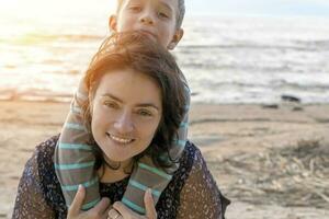 carino contento ragazzo abbracci il suo mamma su il riva del mare nel il tramonto luce. foto