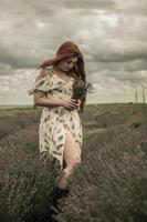 ritratto di una giovane ragazza dai capelli rossi in un abito bianco in un campo con un bouquet di lavanda foto