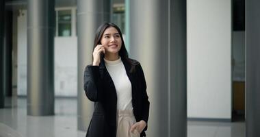 giovane asiatico donna d'affari nel completo da uomo parlando su smartphone mentre a piedi foto