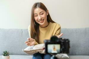 vlogger influencer, attraente asiatico giovane donna blogger, soddisfare creatore guardare a telecamera, registrazione colloquio sedersi su divano, parlare su video tiro sociale media, vivere trasmissione con tecnologia a casa. foto