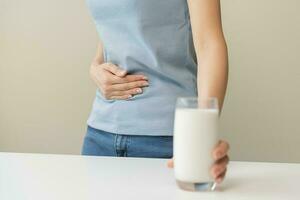 dolore, sofferenza asiatico giovane donna avendo un' mal di stomaco, addominale dolore o digestivo, mano nel Tenere pancia dopo bevanda bicchiere di latte. lattosio intolleranza, allergia a partire dal latteria cibo, Salute cura problema. foto