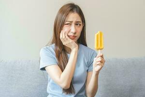 viso espressione sofferenza a partire dal sensibile denti e freddo, asiatico giovane donna, ragazza sensazione male, dolore mangiare ghiaccio crema, lecca lecca. mal di denti molare dente a casa, dentale problema isolato su bianca sfondo. foto