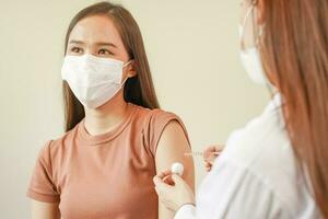 covid19, malattia asiatico giovane donna infermiera ,medico dando siringa vaccino, iniettare tiro per braccia paziente. vaccinazione, immunizzazione o malattia prevenzione contro influenza o virus pandemia concetto. foto