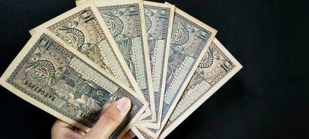 uomo Tenere di vecchio indonesiano banconote rp.10,00 rilasciato nel 1963. vecchio rupia moneta concetto isolato su un' nero sfondo. superiore Visualizza foto