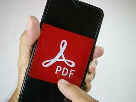 Giacarta, Indonesia, 2023. mano Tenere mobile Telefono con dito toccare il PDF logo su schermo. foto