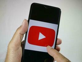 Giacarta, Indonesia, 2023. mano Tenere mobile Telefono con dito toccare il Youtube logo su schermo. foto