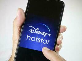 Giacarta, Indonesia, 2023. mano Tenere mobile Telefono con dito toccare il disney hotstar logo su schermo. foto