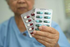 paziente senior asiatico della donna che tiene le pillole della capsula degli antibiotici in imballaggio della bolla per il paziente di infezione del trattamento in ospedale, concetto della farmacia della farmacia. foto