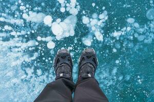 uomo nel stivali in piedi su congelato lago con naturale bolla nel inverno foto