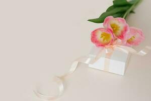 un' mazzo di bellissimo tulipani e un' regalo su un' beige sfondo superiore Visualizza. La madre di giorno sfondo, San Valentino giorno, internazionale Da donna giorno. vacanza, dare un' regalo. foto