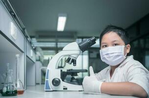 carino asiatico scienziato ragazzo indossare maschera e Lavorando con microscopio nel laboratorio, foto