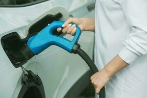 giovane attività commerciale donna rifornimento carburante sua elettrico auto a un' ev ricarica stazione. concetto di l'ambiente amichevole veicolo. elettrico auto concetto. verde in viaggio. foto