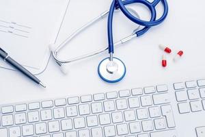 scrivania medico con stetoscopio tastiera del computer e pillole medicinali su sfondo bianco assistenza sanitaria o sfondo concetto farmacia vista dall'alto