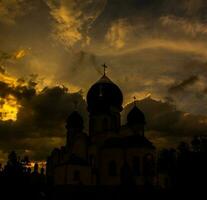 il silhouette di il cupole di un ortodosso cristiano Chiesa nel Romania contro il sfondo di il rosso cielo. fede o religione concetto foto