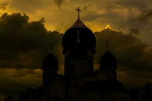 il silhouette di il cupole di un ortodosso cristiano Chiesa nel Romania contro il sfondo di il rosso cielo. fede o religione concetto foto