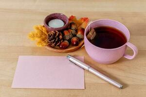 autunno umore composizione su un' di legno tavolo con tè tazza, saluto carta e le foglie. foto