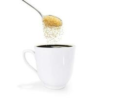 un' cucchiaio di granulato zucchero è versato in un' bianca caffè tazza. isolato su bianca sfondo foto