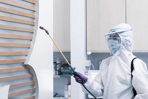 lavoratore in dispositivi di protezione individuale tra cui maschera per tuta bianca e visiera disinfettante sparaying per controllare l'infezione da coronavirus nella clinica del dentista