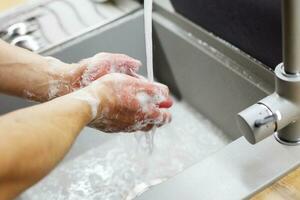 un' uomo lavaggi il suo mani con sapone sotto il rubinetto sotto in esecuzione acqua avvicinamento. Salute, e igiene concetto. foto