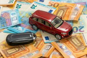 chiave e rosso giocattolo auto su mucchio di Euro banconote, acquistare o vendere un' macchina, affitto un' auto o assicurazione concetto foto