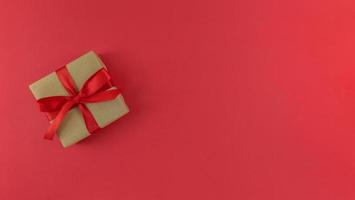 confezione regalo avvolta in una carta artigianale con nastro rosso e fiocco su sfondo rosso piatto festivo monocromatico con spazio per le copie