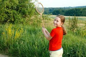 carino poco ragazza con un' Sorridi Tenere un' badminton racchetta nel il campagna foto