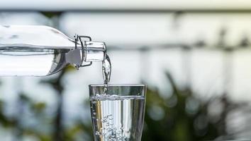 versando l'acqua della bevanda dalla bottiglia nel bicchiere a casa del giardino foto