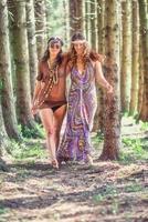 coppia di donne in stile hippie camminano abbracciate nel bosco foto