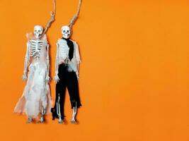 Halloween decorazioni su un arancia sfondo. Due scheletri nel vecchio nozze Abiti, sospeso su il forca. copia spazio foto