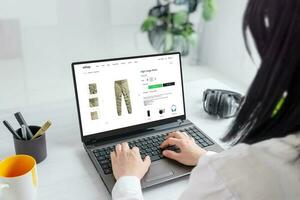 donna navigazione in linea per carico pantaloni, esplorando elegante opzioni e scoperta il Perfetto in forma per sua armadio. moderno e-commerce ragnatela luogo su il computer portatile Schermo foto