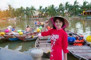 contento donna indossare ao dai vietnamita vestire, viaggiatore visitare gio bon fiume e giro turistico barca cavalcata a Hoi un antico cittadina. punto di riferimento per turista attrazioni.vietnam e sud-est viaggio concetto foto