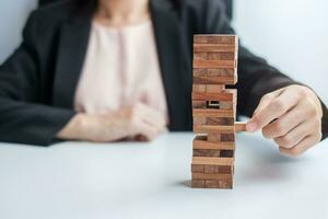 imprenditrice mano mettendo o tirando il blocco di legno sulla torre. concetti di pianificazione aziendale, gestione del rischio, soluzione e strategia foto