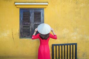 contento donna indossare ao dai vietnamita vestito e cappello, viaggiatore giro turistico a Hoi un antico cittadina nel centrale Vietnam. punto di riferimento e popolare per turista attrazioni. Vietnam e sud-est viaggio concetto foto