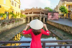 donna viaggiatore indossare ao dai vietnamita vestito giro turistico a giapponese coperto ponte nel Hoi un cittadina, Vietnam. punto di riferimento e popolare per turista attrazioni. Vietnam e sud-est Asia viaggio concetto foto