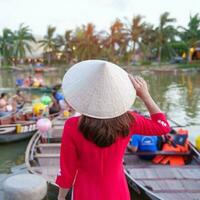 contento donna indossare ao dai vietnamita vestire, viaggiatore visitare gio bon fiume e giro turistico barca cavalcata a Hoi un antico cittadina. punto di riferimento per turista attrazioni.vietnam e sud-est viaggio concetto foto
