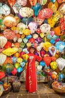 contento donna indossare ao dai vietnamita vestito con colorato lanterne, viaggiatore giro turistico a Hoi un antico cittadina nel centrale vietnam.punto di riferimento per turista attrazioni.vietnam e sud-est viaggio concetto foto