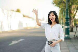 ritratto giovane bellissimo asiatico donna agitando mano per amico di il strada nel soleggiato vacanza. foto
