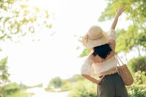 ritratto di asiatico giovane donna viaggiatore con tessitura cappello e cestino e un' telecamera su verde pubblico parco natura sfondo. viaggio viaggio stile di vita, mondo viaggio esploratore o Asia estate turismo concetto. foto