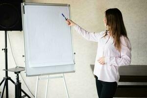 concentrato giovane caucasico altoparlante donna allenatore mostrare su bianca asse, preparazione o dando educativo conferenza. femmina squadra capo spiegando progetto idee. foto