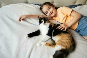 ritratto di un' carino poco ragazza dire bugie su il letto con sua gatto foto