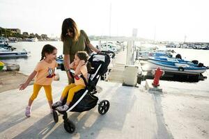 madre con Due bambini nel un' passeggino su il molo di il mare. foto