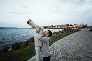 un' ragazzo sembra attraverso un' telescopio a il mare nel il sera. foto